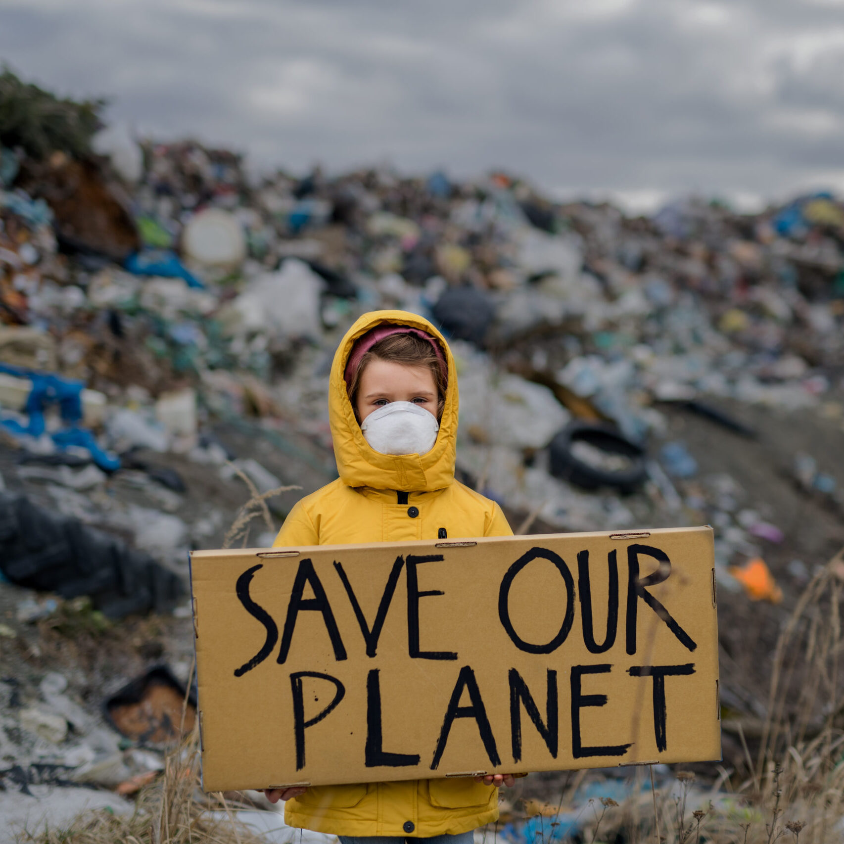 Small child holding placard poster on landfill, environmental pollution concept.